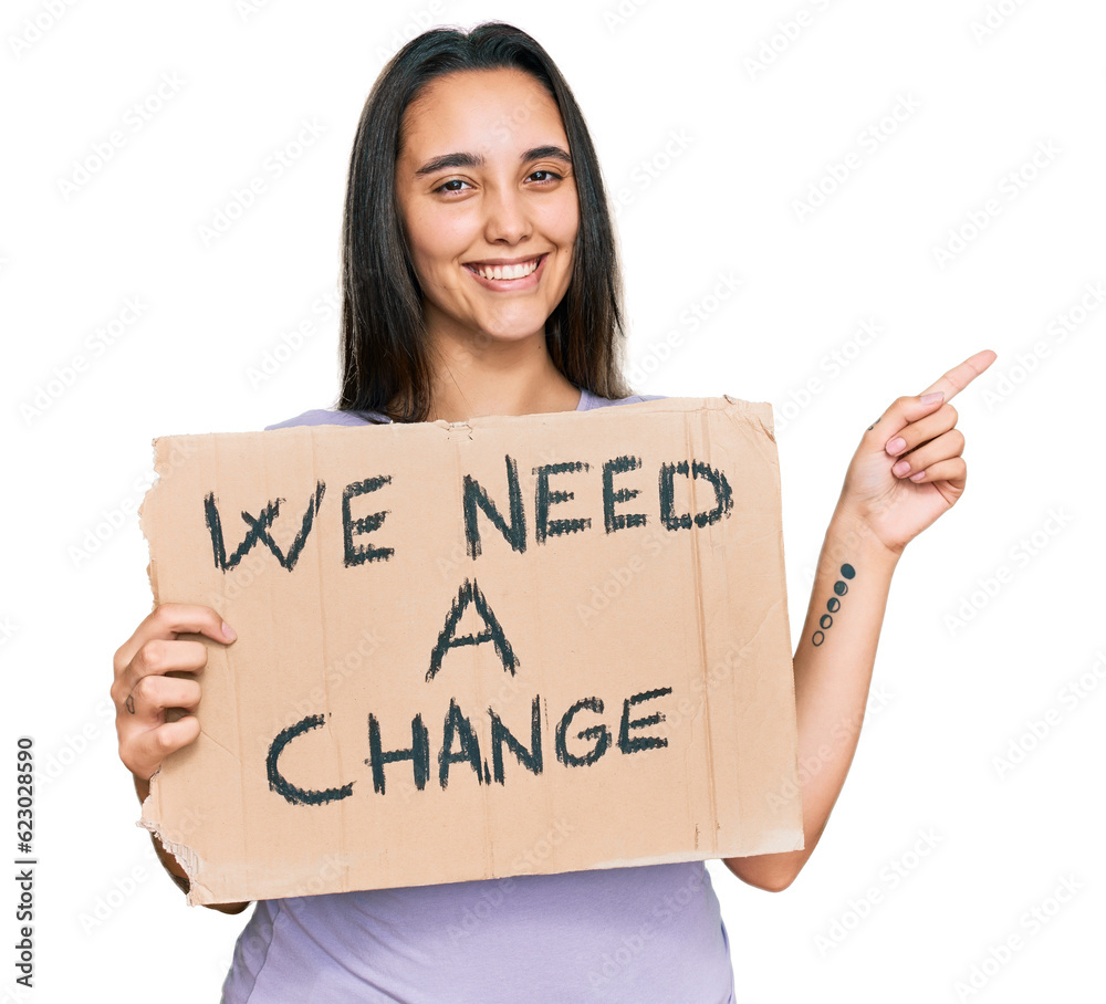 Young hispanic woman holding we need a change banner smiling happy pointing with hand and finger to the side Young hispanic woman holding we need a change banner smiling happy pointing with hand and finger to the side