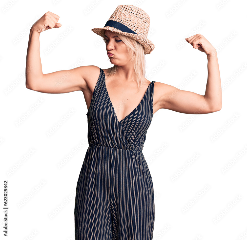 Young beautiful blonde woman wearing summer hat and dress showing arms muscles smiling proud. fitness concept. Young beautiful blonde woman wearing summer hat and dress showing arms muscles smiling proud. fitness concept.