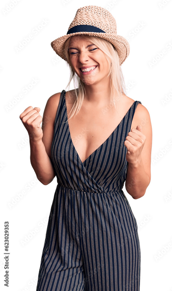 Young beautiful blonde woman wearing summer hat and dress excited for success with arms raised and eyes closed celebrating victory smiling. winner concept. Young beautiful blonde woman wearing summer hat and dress excited for success with arms raised and eyes closed celebrating victory smiling. winner concept.