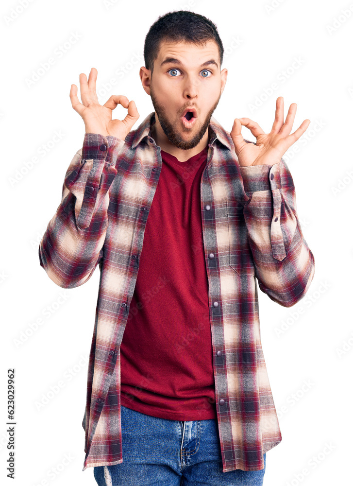 Young handsome man wearing casual shirt looking surprised and shocked doing ok approval symbol with fingers. crazy expression Young handsome man wearing casual shirt looking surprised and shocked doing ok approval symbol with fingers. crazy expression