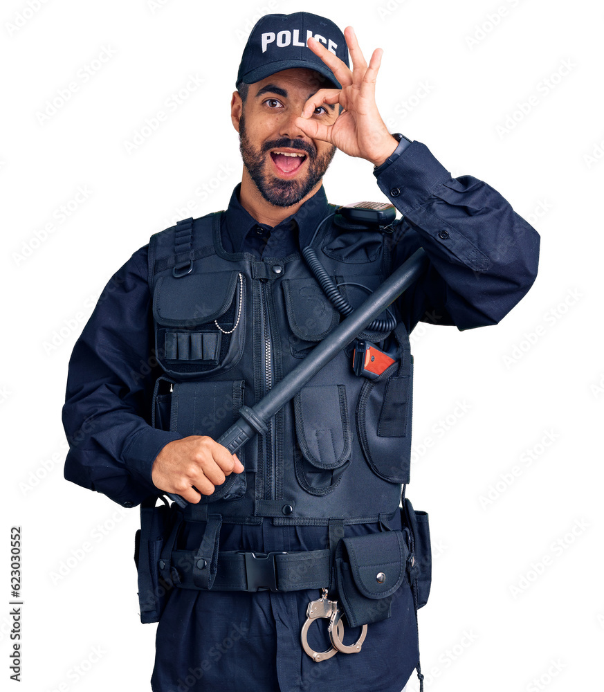 Young hispanic man wearing police uniform holding baton smiling happy doing ok sign with hand on eye looking through fingers Young hispanic man wearing police uniform holding baton smiling happy doing ok sign with hand on eye looking through fingers