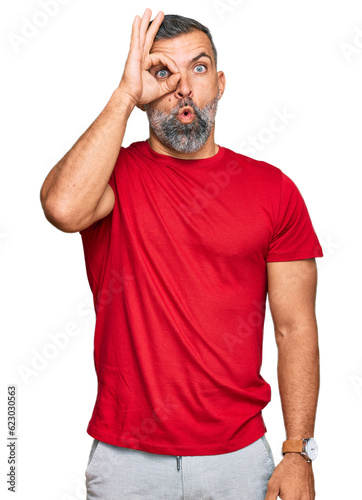 Middle age handsome man wearing casual clothes doing ok gesture shocked with surprised face, eye looking through fingers. unbelieving expression.