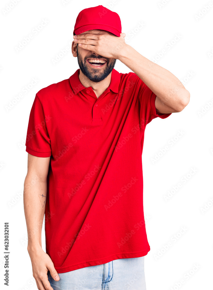Young handsome man with beard wearing delivery uniform smiling and laughing with hand on face covering eyes for surprise. blind concept. Young handsome man with beard wearing delivery uniform smiling and laughing with hand on face covering eyes for surprise. blind concept.