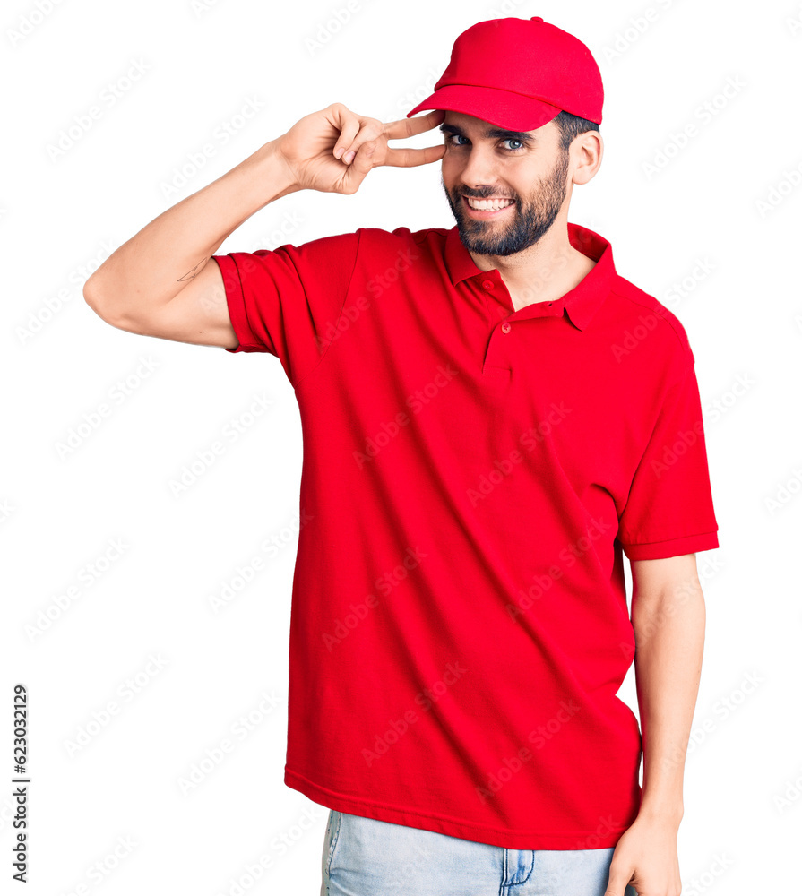 Young handsome man with beard wearing delivery uniform doing peace symbol with fingers over face, smiling cheerful showing victory