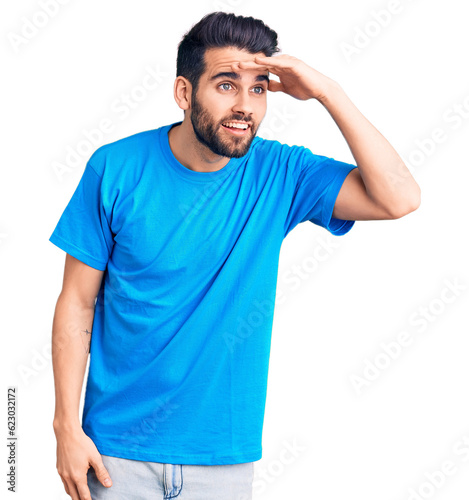 Young handsome man with beard wearing casual t-shirt very happy and smiling looking far away with hand over head. searching concept.