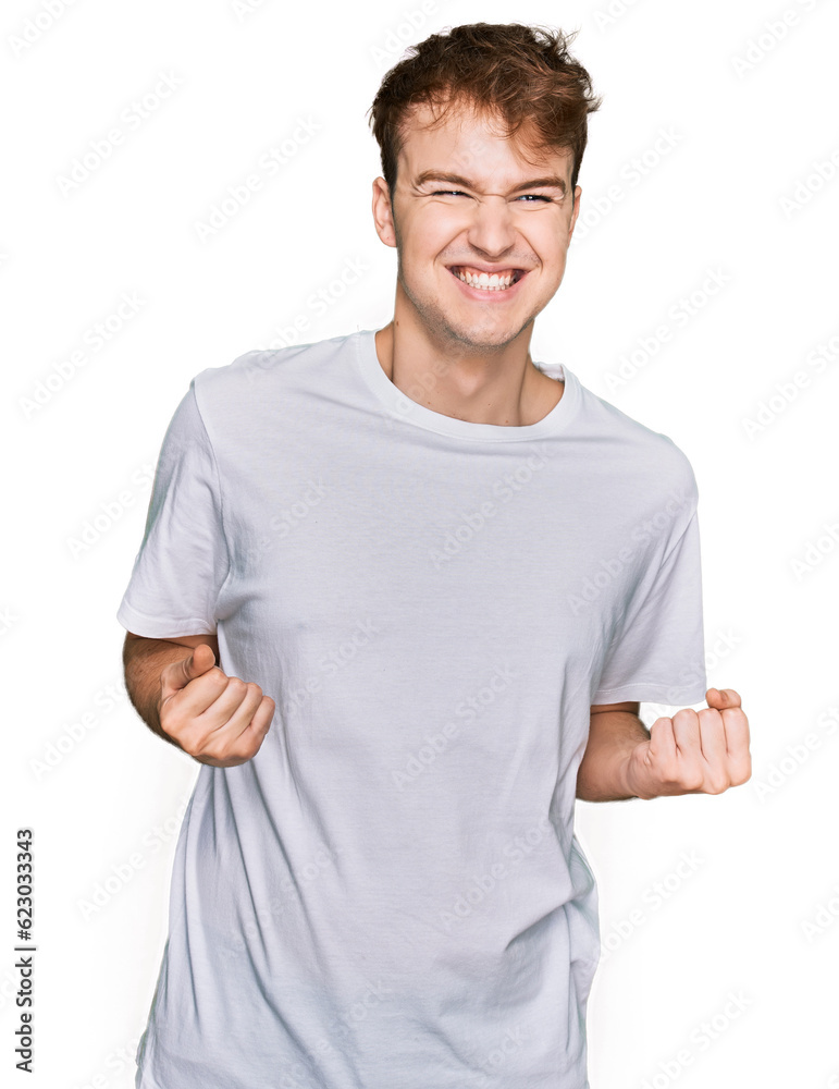 Young caucasian man wearing casual white t shirt excited for success with arms raised and eyes closed celebrating victory smiling. winner concept. Young caucasian man wearing casual white t shirt excited for success with arms raised and eyes closed celebrating victory smiling. winner concept.