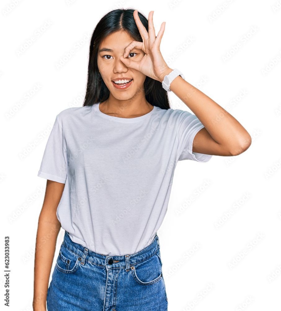 Beautiful young asian woman wearing casual white t shirt doing ok gesture with hand smiling, eye looking through fingers with happy face. Beautiful young asian woman wearing casual white t shirt doing ok gesture with hand smiling, eye looking through fingers with happy face.