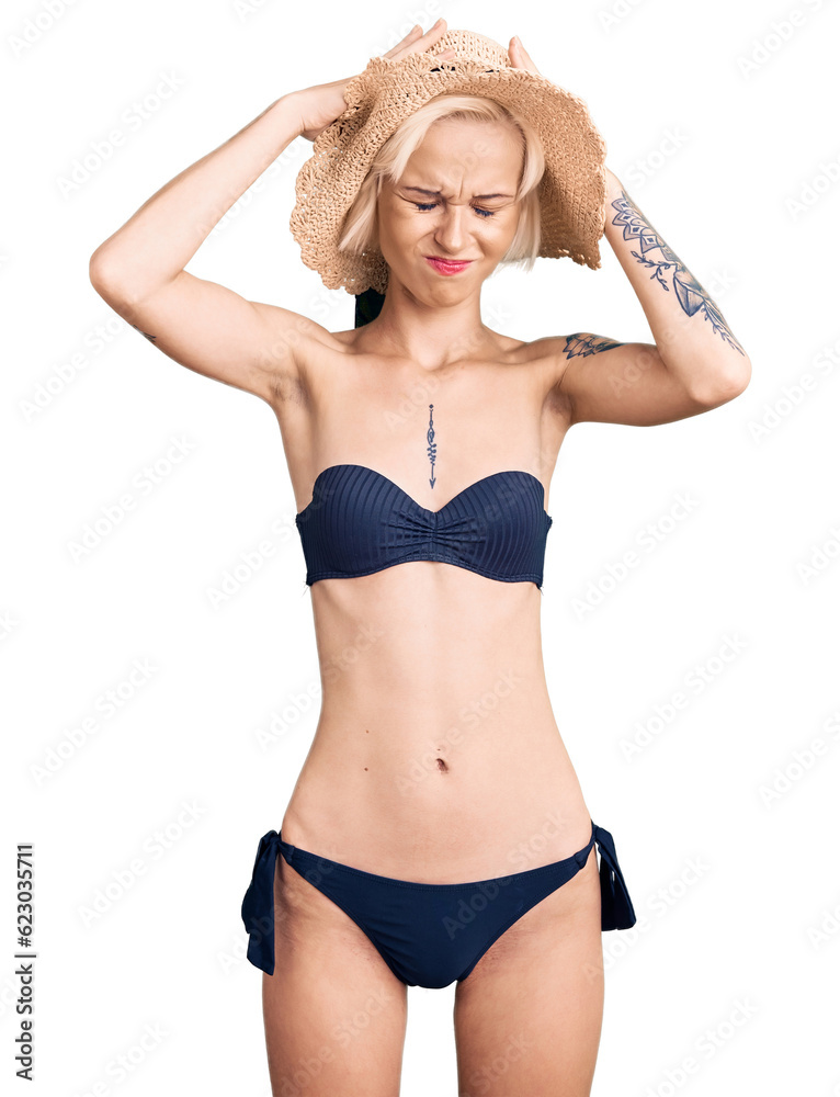 Naklejka premium Young blonde woman with tattoo wearing bikini and summer hat suffering from headache desperate and stressed because pain and migraine. hands on head.