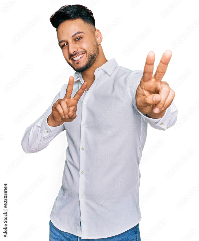 Young arab man wearing casual clothes smiling looking to the camera showing fingers doing victory sign. number two. Young arab man wearing casual clothes smiling looking to the camera showing fingers doing victory sign. number two.