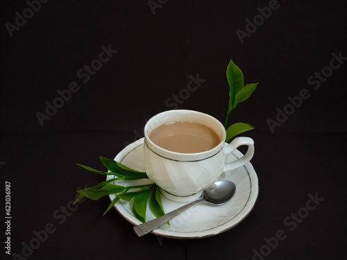 A cup of Traditional Indian milk tea with tea leaves and spoon.