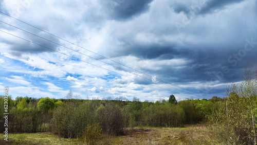 Dark, stormy and rainy clouds over green trees and big field on a spring or summer day