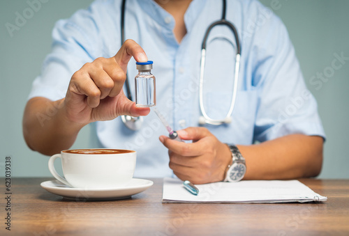 Physician holding a vaccine bottle and a syringe while sitting at the table.
