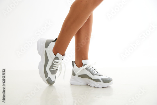 Beautiful white sneakers and woman legs in the studio on white background. Fashionable shooting of a young girl with beautiful legs
