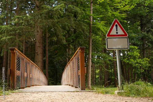 A wooden bridge in the park and a road danger sign.
