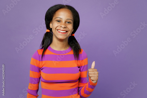 Little smiling kid teen girl of African American ethnicity 15-16 year old wear striped orange sweatshirt showing thumb up like gesture isolated on plain purple background. Childhood lifestyle concept.