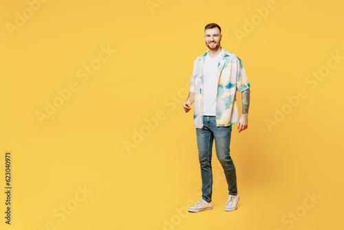Full body sideways smiling cheerful fun cool young man he wear blue shirt white t-shirt casual clothes look camera walking going isolated on plain yellow background studio portrait. Lifestyle concept.