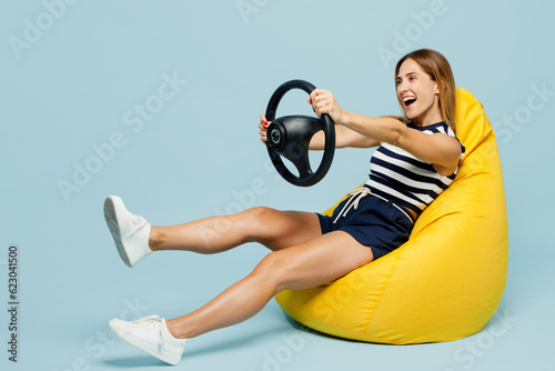 Full body young woman she wear striped tank shirt casual clothes sit in bag chair hold steering wheel driving car isolated on plain pastel light blue cyan background studio portrait Lifestyle concept photo
