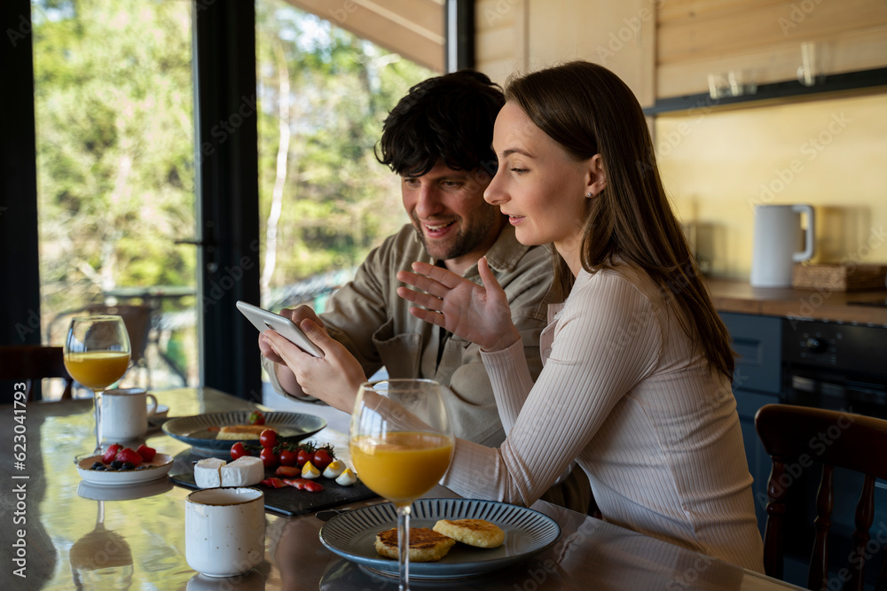 Young beautiful couple in the dining room. A family of two people use a tablet computer while sitting at the dining table Young beautiful couple in the dining room. A family of two people use a tablet computer while sitting at the dining table