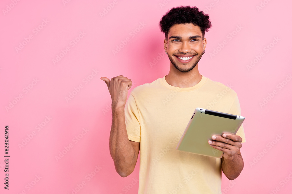 Photo of toothy beaming guy with earrings dressed yellow t-shirt hold tablet indicating empty space isolated on pink color background