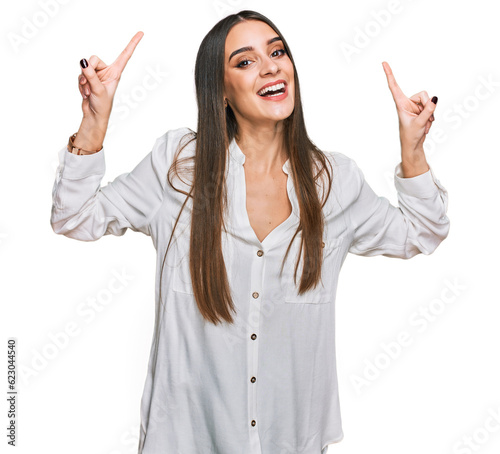 Young beautiful woman wearing casual white shirt smiling amazed and surprised and pointing up with fingers and raised arms.