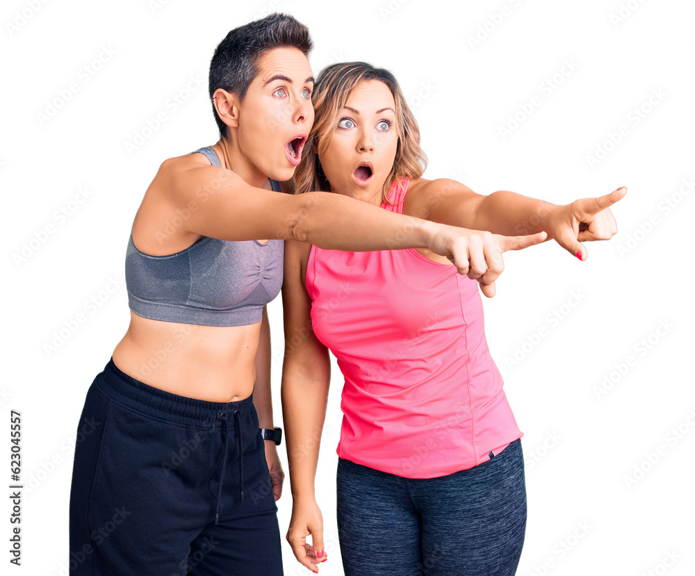 Couple of women wearing sportswear pointing with finger surprised ahead, open mouth amazed expression, something on the front Couple of women wearing sportswear pointing with finger surprised ahead, open mouth amazed expression, something on the front