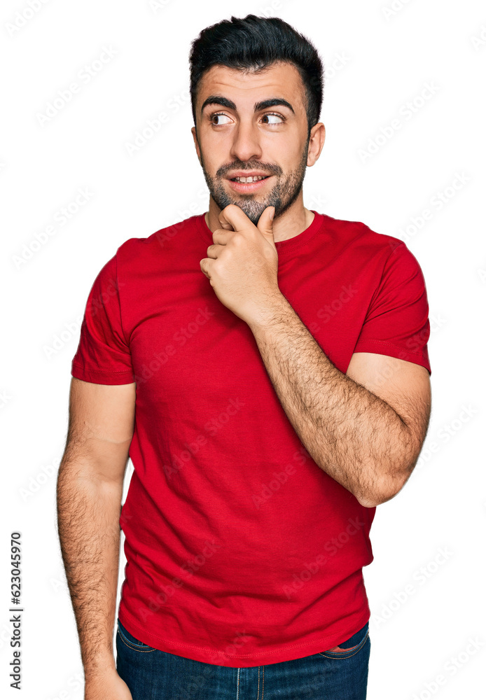 Hispanic man with beard wearing casual red t shirt with hand on chin thinking about question, pensive expression. smiling with thoughtful face. doubt concept. Hispanic man with beard wearing casual red t shirt with hand on chin thinking about question, pensive expression. smiling with thoughtful face. doubt concept.