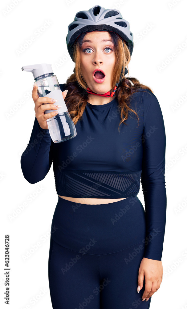 Young beautiful caucasian woman wearing bike helmet and holding water bottle scared and amazed with open mouth for surprise, disbelief face Young beautiful caucasian woman wearing bike helmet and holding water bottle scared and amazed with open mouth for surprise, disbelief face