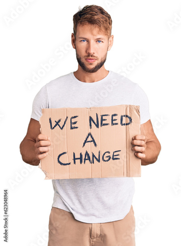 Young caucasian man holding we need a change banner thinking attitude and sober expression looking self confident