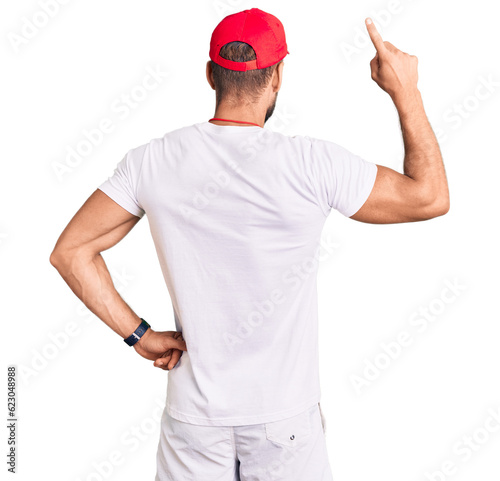 Young caucasian man wearing lifeguard t shirt holding whistle posing backwards pointing ahead with finger hand