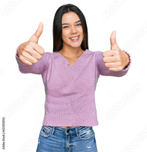 Young hispanic girl wearing casual clothes approving doing positive gesture with hand, thumbs up smiling and happy for success. winner gesture.
