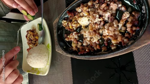 Candid moment of a tourist de-seeding calamasi to be squeezed on a pork sisig with rice, an authentic traditional Filipino dish originally a Kapampangan delicacy, vertical overhead view