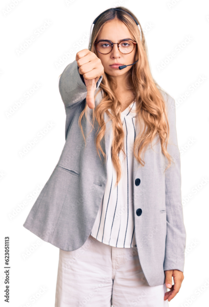 Young beautiful blonde woman wearing call center agent headset looking unhappy and angry showing rejection and negative with thumbs down gesture. bad expression. Young beautiful blonde woman wearing call center agent headset looking unhappy and angry showing rejection and negative with thumbs down gesture. bad expression.
