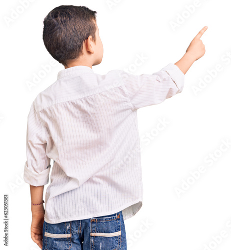 Cute blond kid wearing elegant shirt posing backwards pointing ahead with finger hand