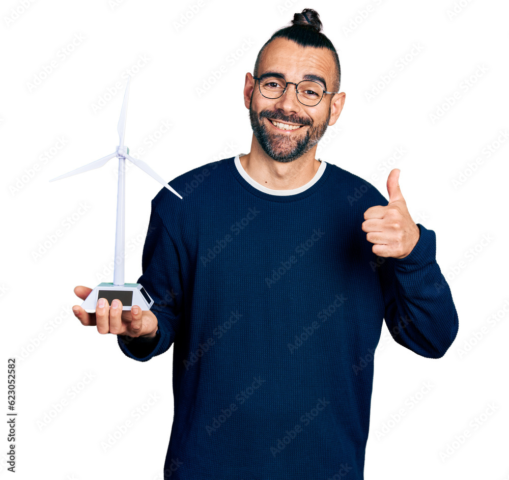 Hispanic man with ponytail holding solar windmill for renewable electricity smiling happy and positive, thumb up doing excellent and approval sign Hispanic man with ponytail holding solar windmill for renewable electricity smiling happy and positive, thumb up doing excellent and approval sign