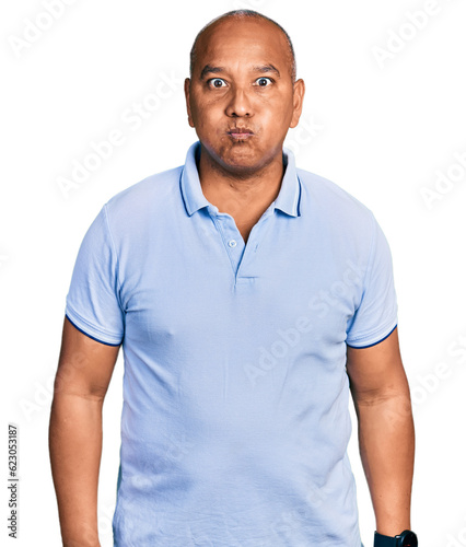 Hispanic middle age man wearing casual t shirt puffing cheeks with funny face. mouth inflated with air, crazy expression.