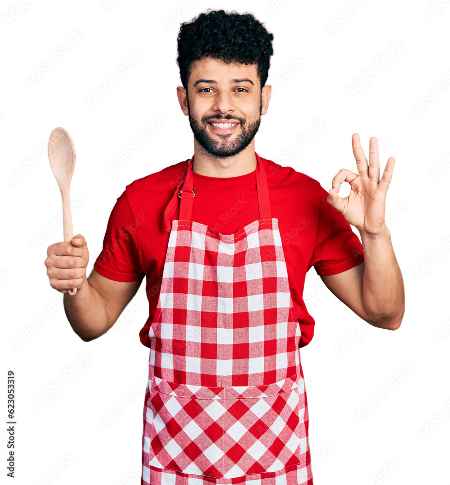 Young arab man with beard wearing baker uniform holding wooden spoon smiling with a happy and cool smile on face. showing teeth. Young arab man with beard wearing baker uniform holding wooden spoon smiling with a happy and cool smile on face. showing teeth.