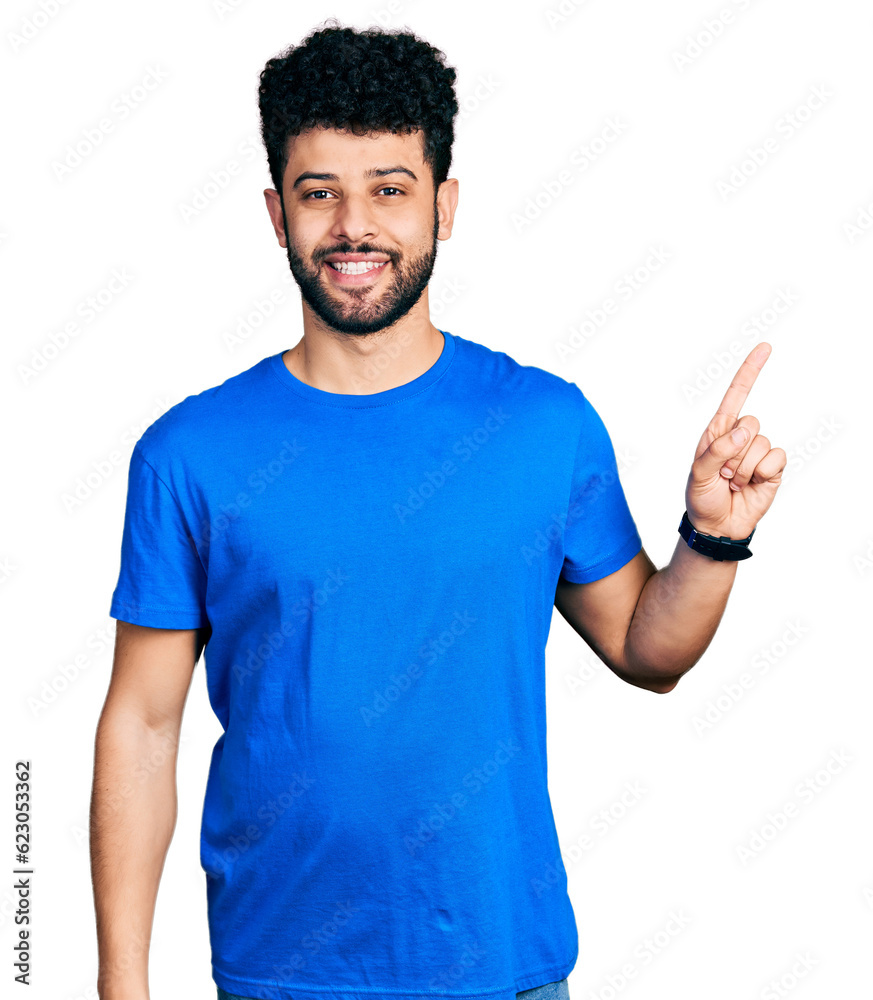 Fototapeta premium Young arab man with beard wearing casual blue t shirt with a big smile on face, pointing with hand finger to the side looking at the camera.