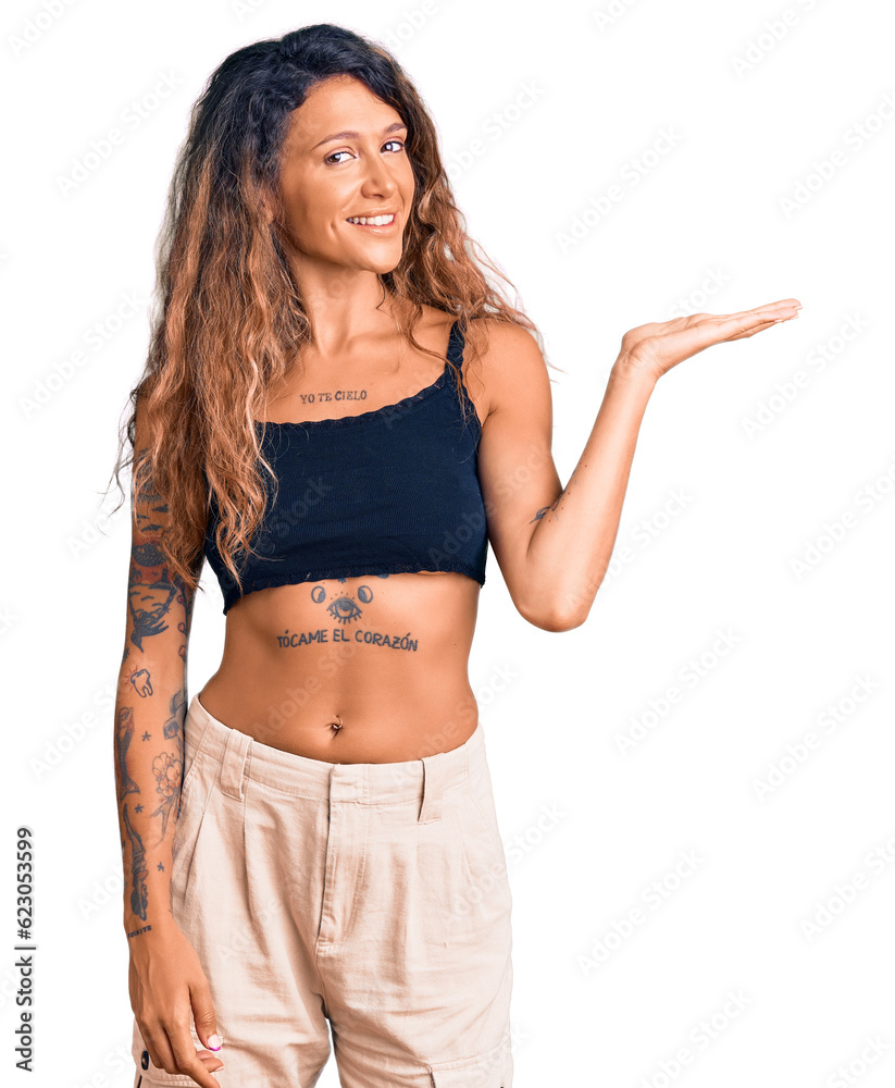 Young hispanic woman with tattoo wearing casual clothes smiling cheerful presenting and pointing with palm of hand looking at the camera. Young hispanic woman with tattoo wearing casual clothes smiling cheerful presenting and pointing with palm of hand looking at the camera.