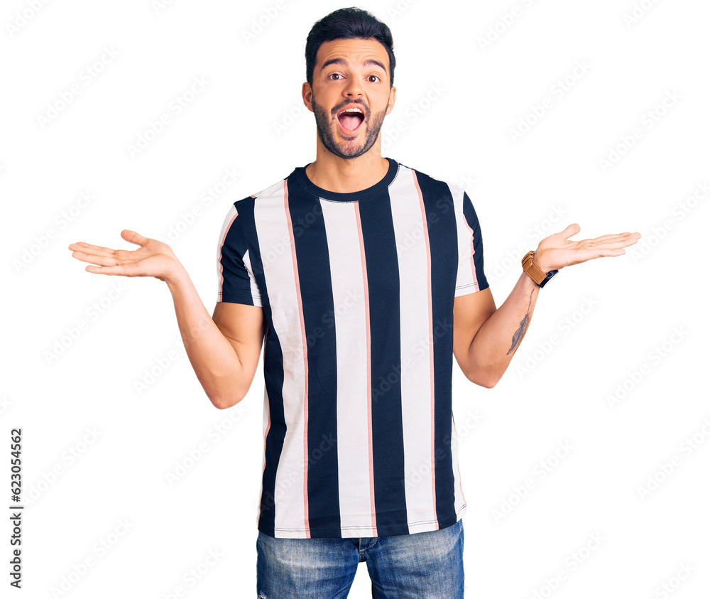 Young handsome hispanic man wearing striped tshirt celebrating crazy and amazed for success with arms raised and open eyes screaming excited. winner concept Young handsome hispanic man wearing striped tshirt celebrating crazy and amazed for success with arms raised and open eyes screaming excited. winner concept