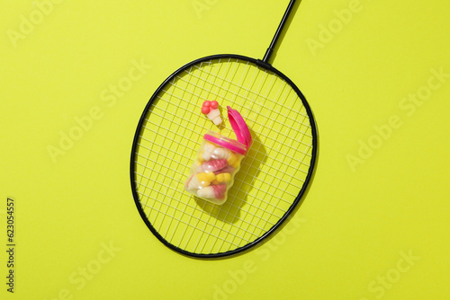 Jelly candies in jar on tennis racket on green background, top view photo