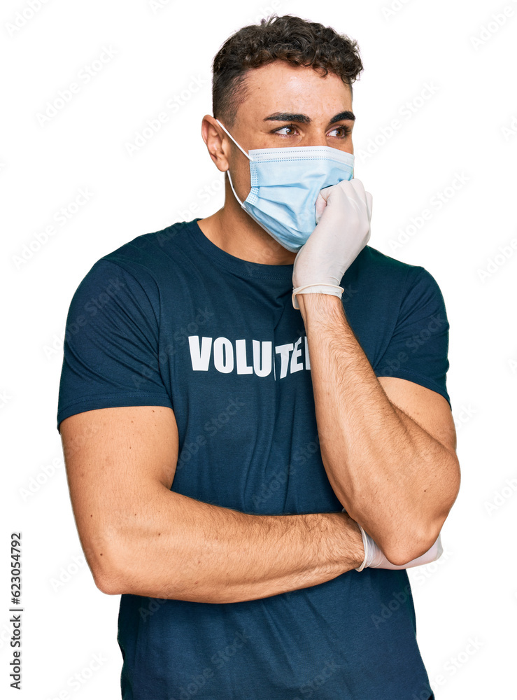 Hispanic young man wearing medical mask and volunteer t shirt looking stressed and nervous with hands on mouth biting nails. anxiety problem. Hispanic young man wearing medical mask and volunteer t shirt looking stressed and nervous with hands on mouth biting nails. anxiety problem.
