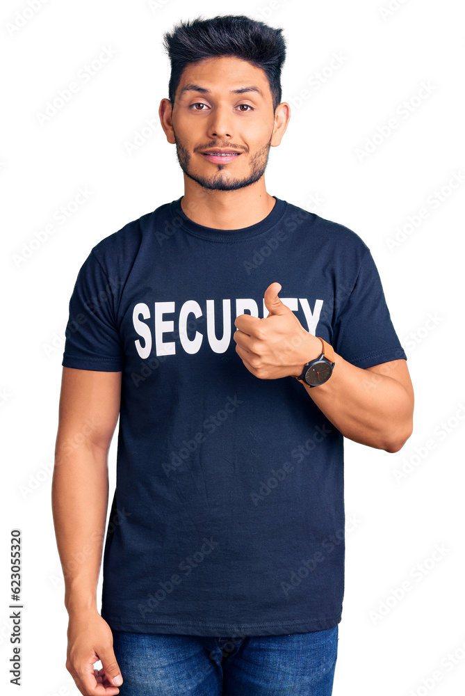 Handsome latin american young man wearing security t shirt doing happy thumbs up gesture with hand. approving expression looking at the camera showing success. Handsome latin american young man wearing security t shirt doing happy thumbs up gesture with hand. approving expression looking at the camera showing success.