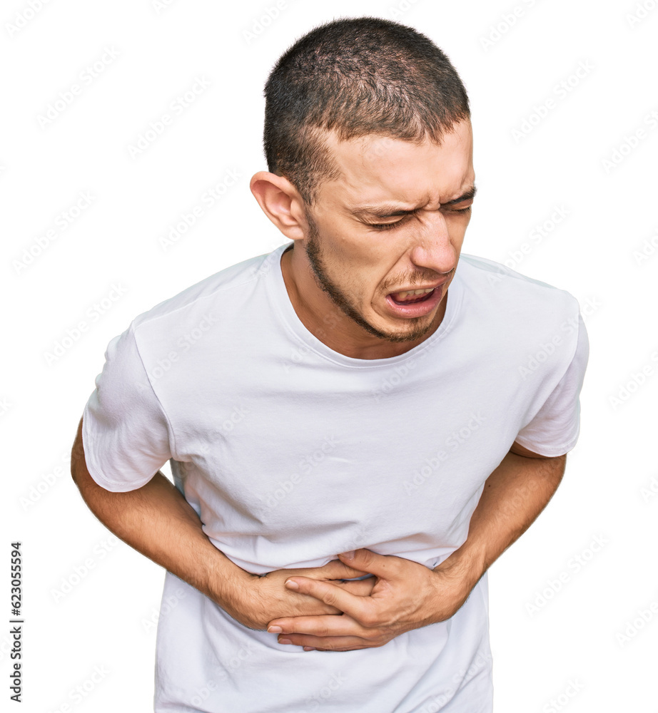 Hispanic young man wearing casual white t shirt with hand on stomach because nausea, painful disease feeling unwell. ache concept. Hispanic young man wearing casual white t shirt with hand on stomach because nausea, painful disease feeling unwell. ache concept.