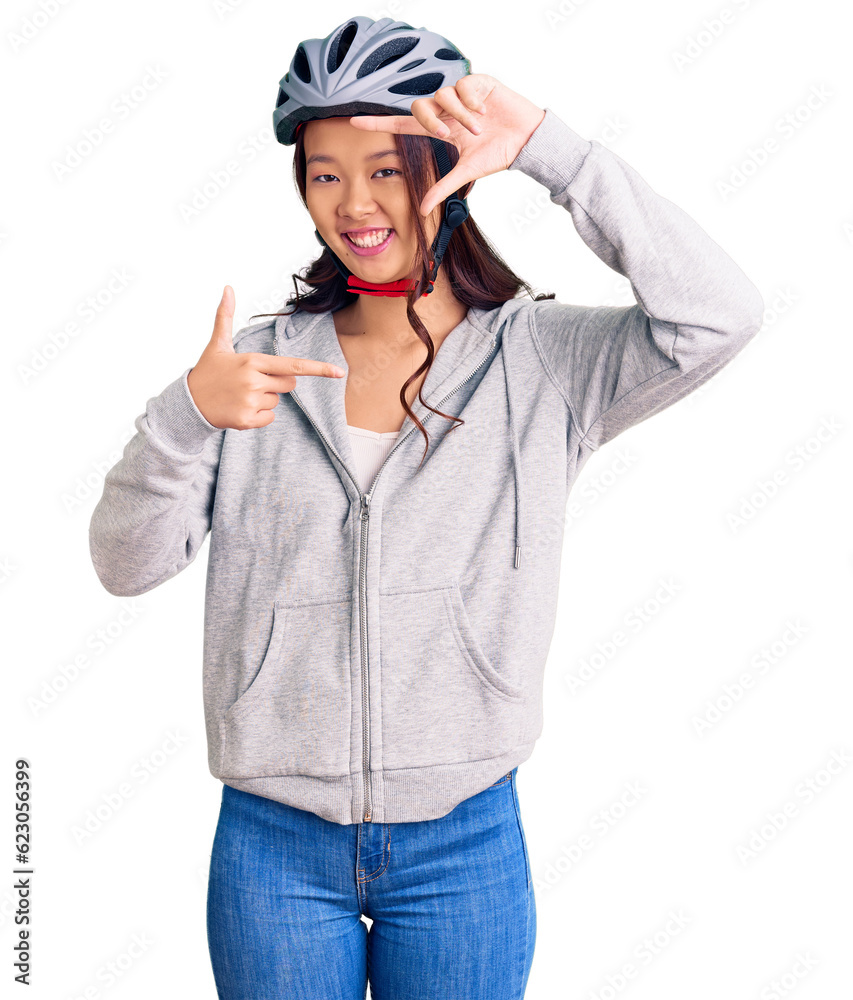 Young beautiful chinese girl wearing bike helmet smiling making frame with hands and fingers with happy face. creativity and photography concept. Young beautiful chinese girl wearing bike helmet smiling making frame with hands and fingers with happy face. creativity and photography concept.