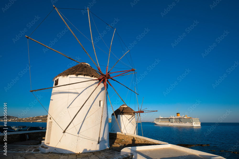 Scenic view of famous Mykonos town windmills. Traditional greek windmills on Mykonos island at sunrise with cruise ship in background, Cyclades, Greece