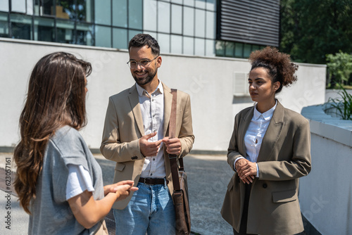 Group of business people walk outside in front of office buildings. Businessman and two businesswomen sharing experience ideas and tactic for successful strategy and marketing. Workers taking a break.