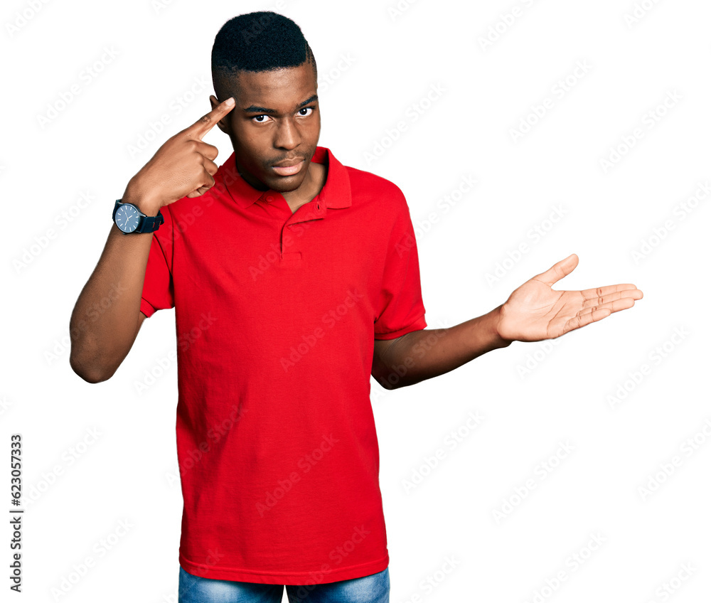 Young african american man wearing casual red t shirt confused and annoyed with open palm showing copy space and pointing finger to forehead. think about it. Young african american man wearing casual red t shirt confused and annoyed with open palm showing copy space and pointing finger to forehead. think about it.