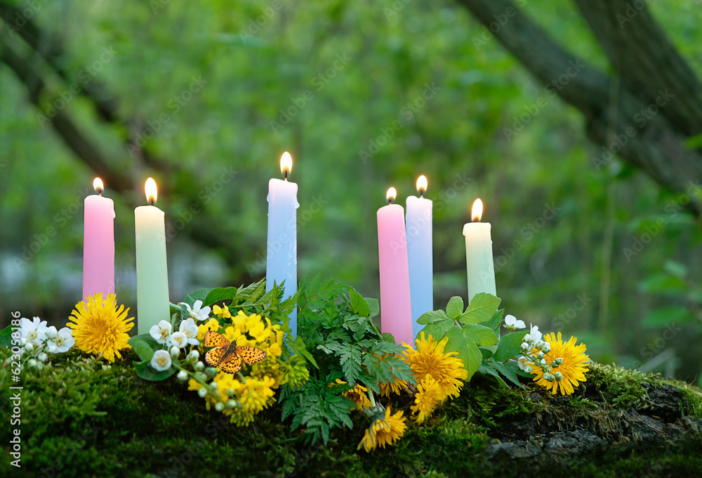 colorful magic candles and flowers in forest, blurred natural