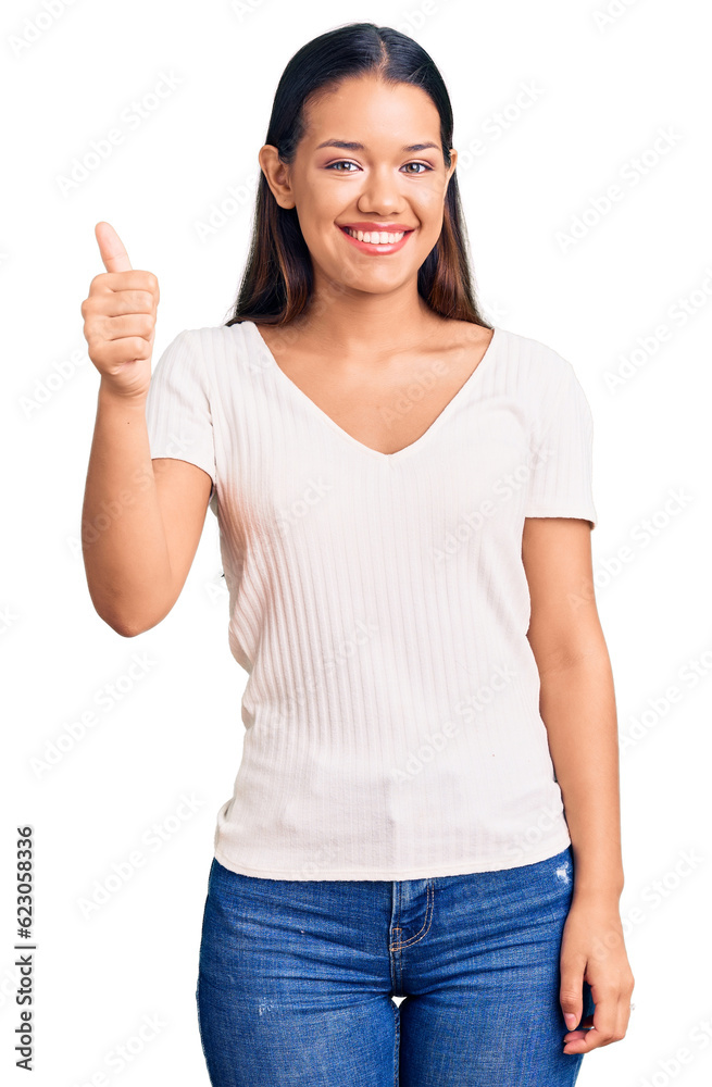 Young beautiful latin girl wearing casual white t shirt smiling happy and positive, thumb up doing excellent and approval sign Young beautiful latin girl wearing casual white t shirt smiling happy and positive, thumb up doing excellent and approval sign