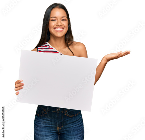 Beautiful hispanic woman holding blank empty banner celebrating victory with happy smile and winner expression with raised hands